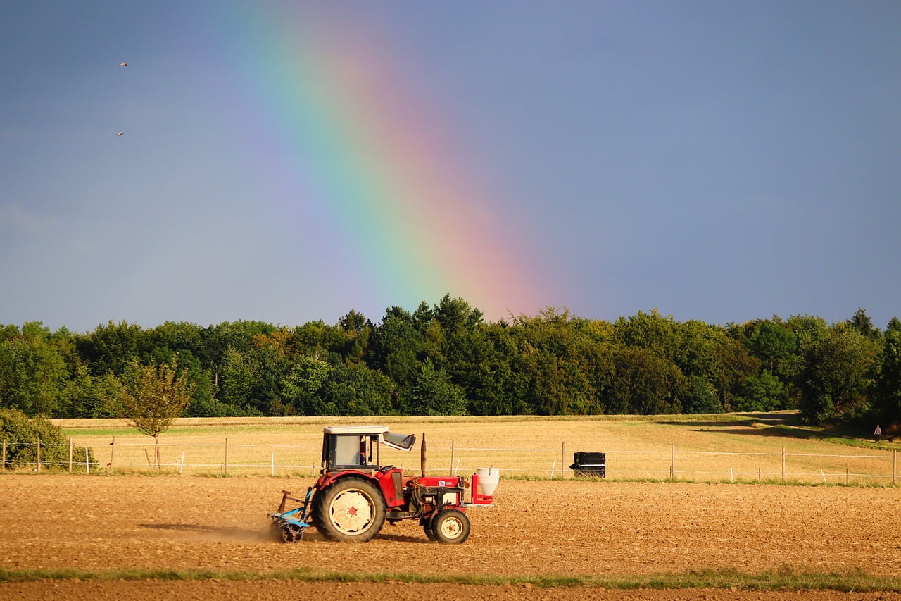 traktor na polu, tęcza w tle